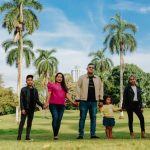 A cheerful family enjoys a sunny day in the park, surrounded by palm trees and lush greenery.